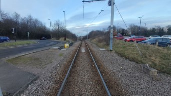 Lay-by meeting the road, tram line off into the distance, parked cars.