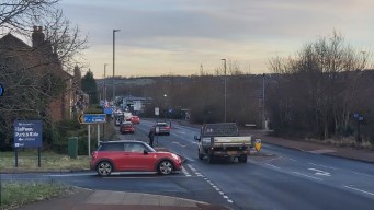 A straight, busy road with a petrol station, and a post indicating a bus stop.
